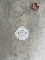 May include: A white circle sticker with a black border and black clock hands. The sticker has the text 'Sore but Cute' in pink and black text with two black diamond shapes on either side of the text.